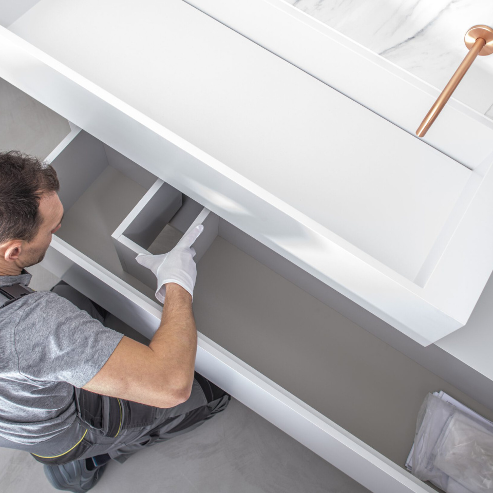 Installateur montiert weißen Badezimmerschrank unter Waschbecken