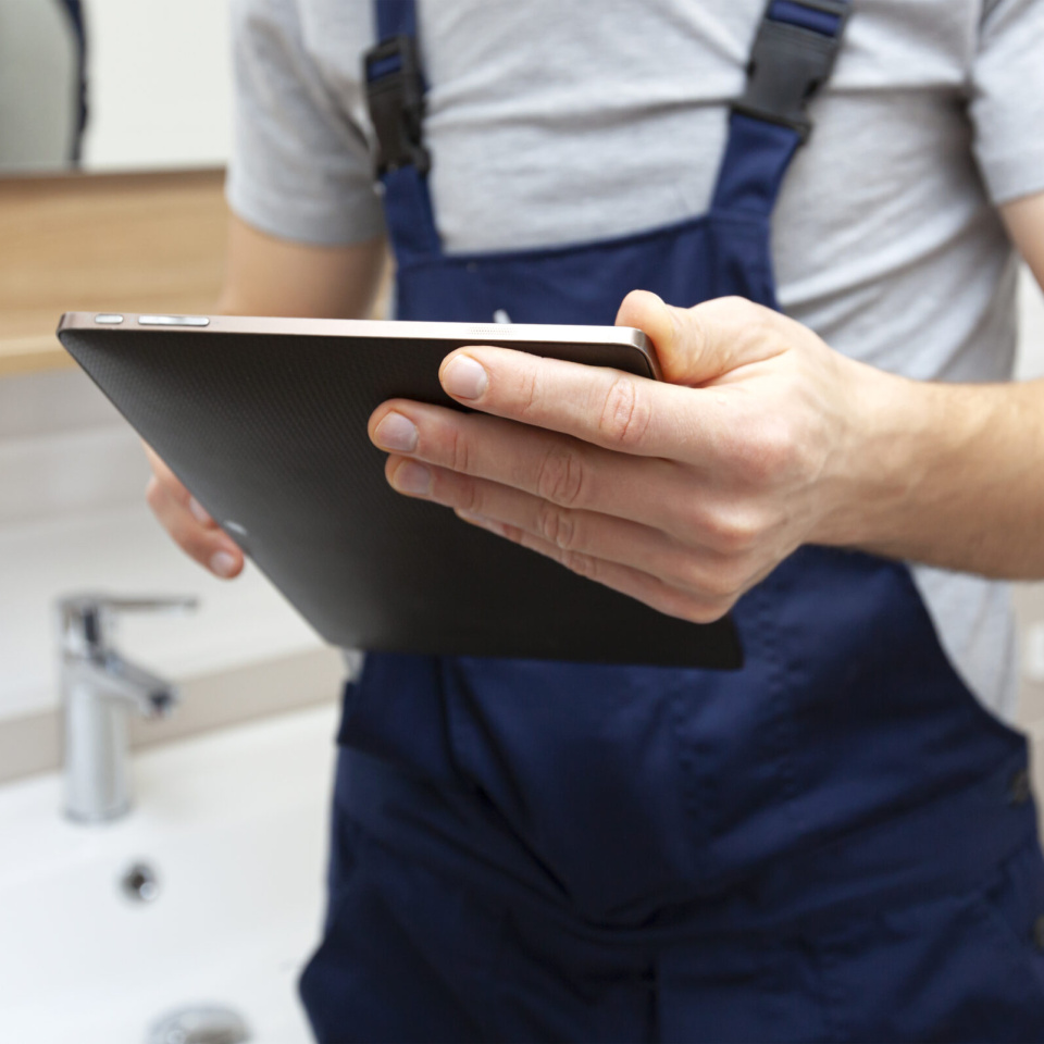 Installateur in Arbeitskleidung hält Tablet über Waschbecken